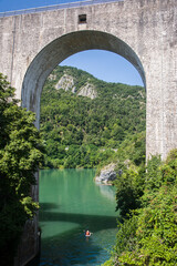 Fototapeta premium Un couple sur un canoe kayak sur l'Isère. Un loisir nautique sous un pont avec des arches. Saint-Nazaire-en-Royans. La Drome. L'Isère. Les vacances à la montagne en France. Des vacances à la campagne.