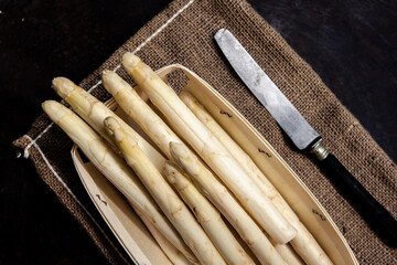 Asperges blanches dans une barquette en bois et un couteau, vu de dessus