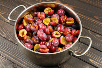 Textured surface, Metal pan with berries with chopped ripe plums for cooking jam, on wooden surface