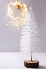 Fototapeta na wymiar New Year decorations. Decorative white holiday tree and festive bokeh lights on grey textured background. Scandinavian minimalistic style. Still life.