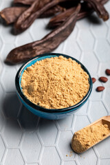 Carob pods and carob powder over a blue background.