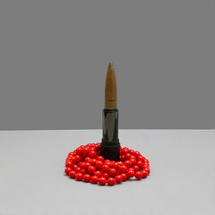 Bullet in lipstick with vibrant red pearl necklace on grey backround. Feminine background for...