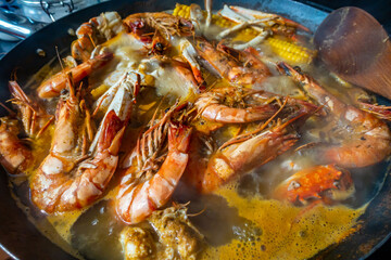 Seafood boil with crabs, prawns and corn on the cob boiling in a wok on a hob in a home kitchen.