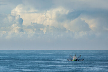 A cutter with lifted drag nets on the blue water of the North sea with sunny clouds