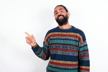 Naklejka premium Emotive Caucasian man with beard wearing sweater over white background keeps jaw dropped from shock demonstrates amazing promo points right on blank space demonstrates big shopping sale. Advertisement