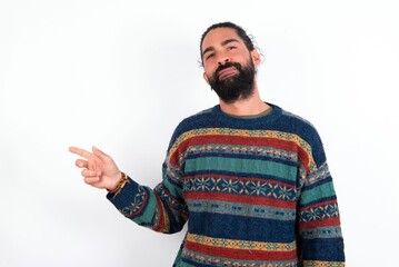 Naklejka premium Serious Caucasian man with beard wearing sweater over white background smirks face points away on copy space shows something unpleasant. Look at this advertisement. Big price concept