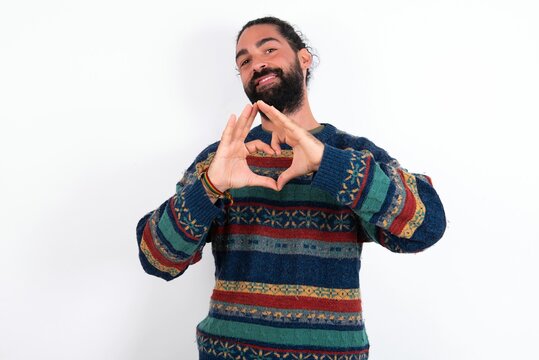 Serious Caucasian man with beard wearing sweater over white background keeps hands crossed stands in thoughtful pose concentrated somewhere