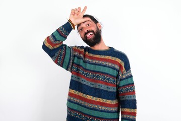 Funny Caucasian man with beard wearing sweater over white background makes loser gesture mocking at...