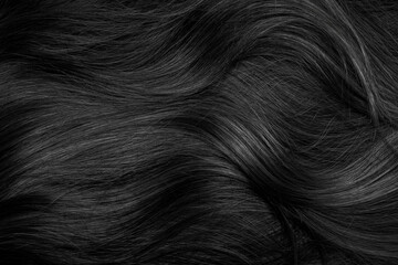 Brunette or black hair. Female long dark hair in black. Beautifully laid curls. Closeup texture in a dark key. Hairdressing, hair care and coloring. Shading gray hair. Background with copy space.