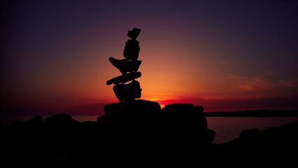 Silhouette of balanced zen stones on the ocean beach ant sunset sunrise time.