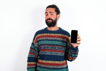 Photo of interested Caucasian man with beard wearing sweater over white background hold telephone look side empty space screen