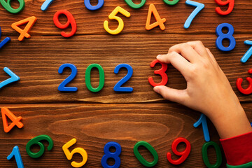 Child hand puts colored numbers 2023 new year on wooden background