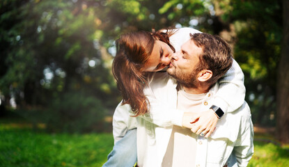 Happy playful couple in love outdoors young woman kissing her boyfriend and enjoying piggyback. © Barillo Images