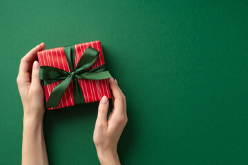 New Year concept. First person top view photo of girl's hands holding red giftbox with ribbon bow on isolated green background with copyspace