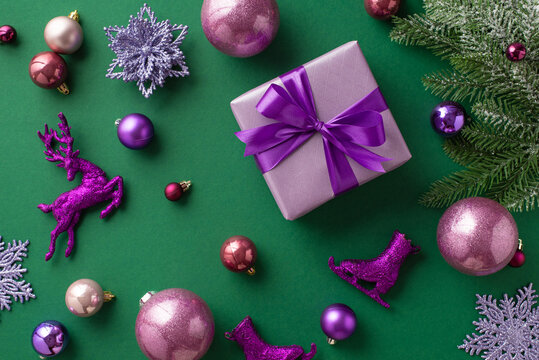 New Year concept. Top view photo of lilac giftbox with violet ribbon bow pink purple baubles reindeer ice skates flower snowflake ornaments and fir branch i hoarfrost on isolated green background