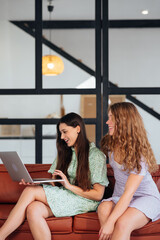 Two young women using computer while sitting on couch.