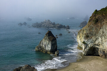 A view looking down on Rainbow Beach towards the southern end of the Samuel H. Boardman State Scenic Corridor, on Oregon's southern coast. It is on a foggy day close to high tide.