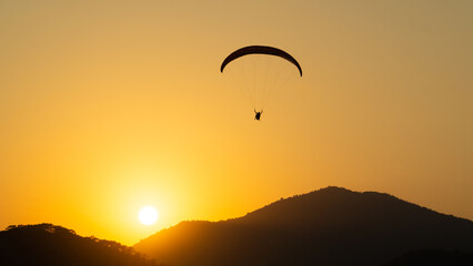 Mountainous landscape at sunset with the contrasting silhouette of a paraglider flying in the sky.