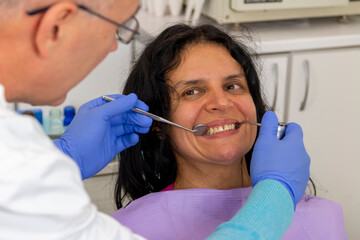 Fototapeta premium A middle-aged woman sitting in medical chair while dentist fixing her teeth at dental clinic