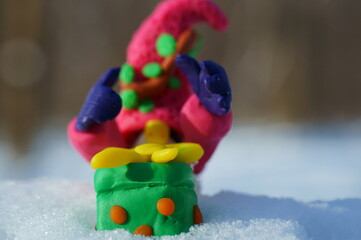 The fairy-tale gnome rejoices at the advent of the New Year holidays. Next to the gift box made of plasticine.
