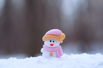A small toy snowman in a hat and scarf on a background of snow.