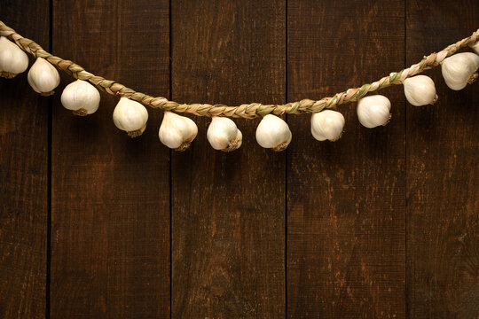 garlic bulbs braided in a pigtail like a garland on a background of dark wooden boards, an empty place for text