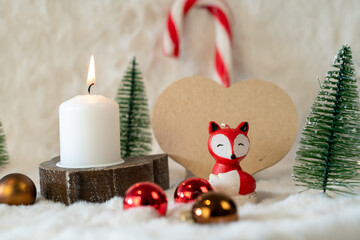 Petite bougie en forme de renard à coté d'une bougie allumée dans un décor de Noël