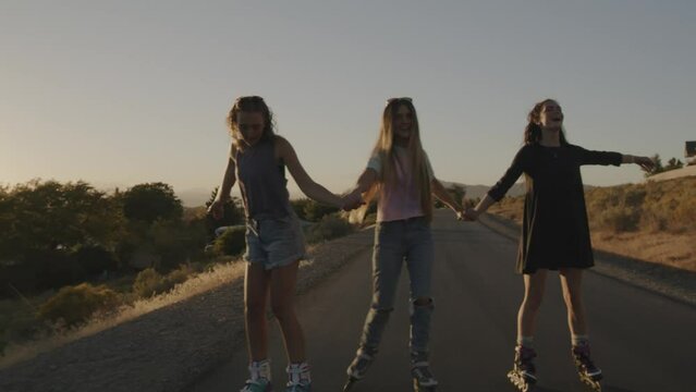Carefree playful girls holding hands and inline skating on park path / Cedar Hills, Utah, United States