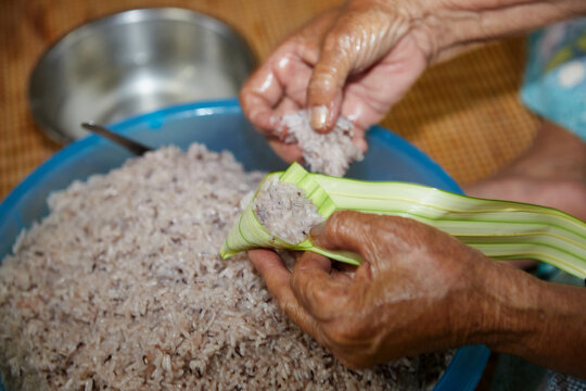 Hands of  senior woman wrapping the sticky rice with palm leaf or Ketupat Palas	