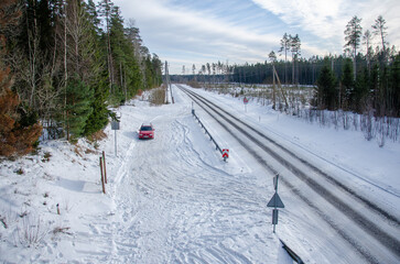 a lone red car on the side of the road near a forest in winter