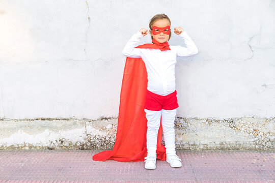 Little girl in superhero costume showing muscles against wall