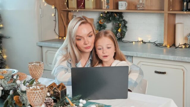 Cute beautiful blond mother with blue eyes and daughter watching video on laptop making online shopping, Christmas Eve sale. Spending quality time with family at Christmas holiday, new year concept.
