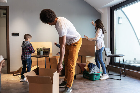 Mixed race family moving into their new home. They're carrying cardboard full of their accessories.