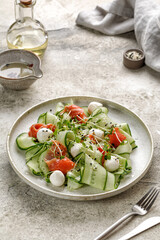 Diet salad with salmon, sliced cucumbers, mozzarella cheese, microgreens on grey ceramic plate and stone background. Healthy dinner concept.