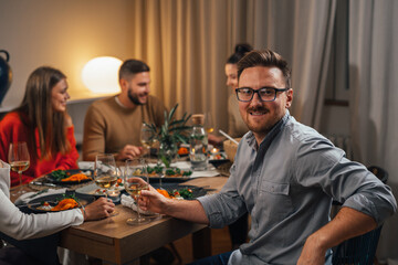 man sits at the table and looks at the camera while having dinner with friends