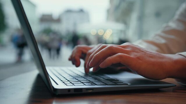 Close-up male hands typing on laptop man freelancer sitting in cafe working remotely outdoors businessman student uses computer technology to study or work online traveler booking ticket in internet