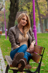 Portrait of a young woman with long blonde hair sitting on a bench in a park