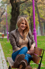 Portrait of a young woman with long blonde hair sitting on a bench in a park