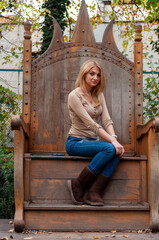 Portrait of a young woman with long blonde hair sitting on a big wooden throne. Sad face.