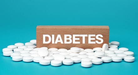 Diabetes word on wooden block with white tablets diabetes pills on blue background. Drug use and...