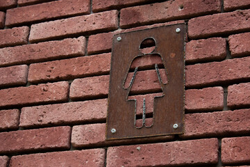 Metal rusty female toilet symbol on the brick wall of the loft. Icon with a girl in a dress. Public toilet in the park. Comfortable urban environment and care for citizens