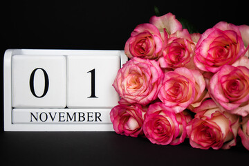  November 1 wooden calendar, white on a black background, pink roses lie nearby.Postcard with copy space. The concept of a holiday, congratulation, invitation, party, announcement, vacation,promotion.