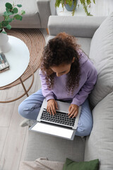 Young African-American woman using laptop on sofa at home, top view