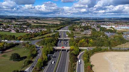 Aerial drone photo of the busy M1 motorway with three bridges crossing over the highway in the village of Barnsley in Sheffield UK in the summer time on a bright sunny summers day. - obrazy, fototapety, plakaty