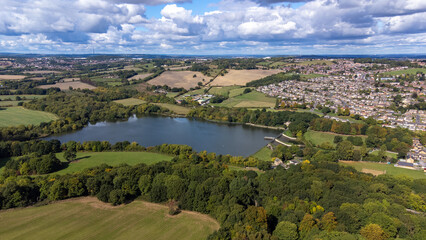 Fototapeta na wymiar Aerial drone photo of the large Worsbrough reservoir in the village of Worsbrough, Barnsley in Sheffield in the UK, showing the British village and housing estates in the summer time