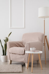 Interior of light living room with beige armchair, table and lamp