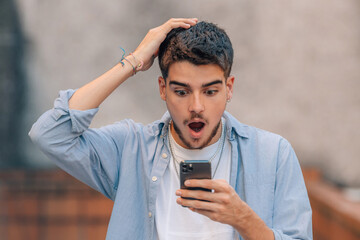 young man looking surprised with mobile phone in the street