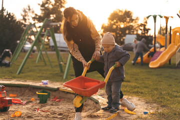 Mother and child playing with wheelbarrow in sandbox. Little builder. Education, and imagination,...