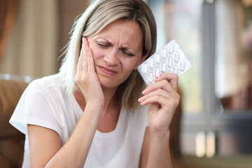 Young woman suffering from tooth pain and holding blister of pills