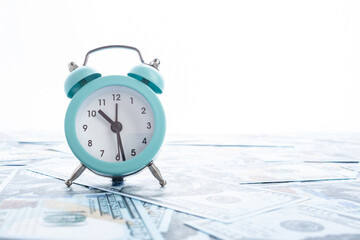 A small alarm clock stands on dollar bills.